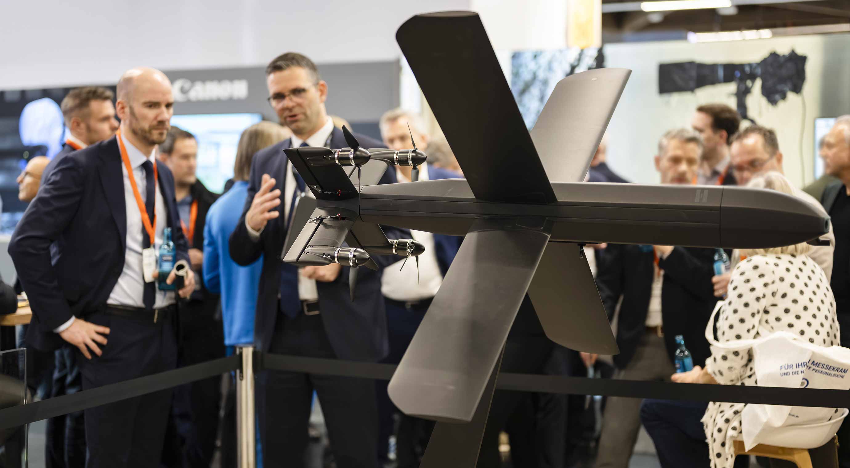 Präsentation einer Drohne am Messestand, Fachpublikum betrachtet unbemanntes Luftfahrzeug.
