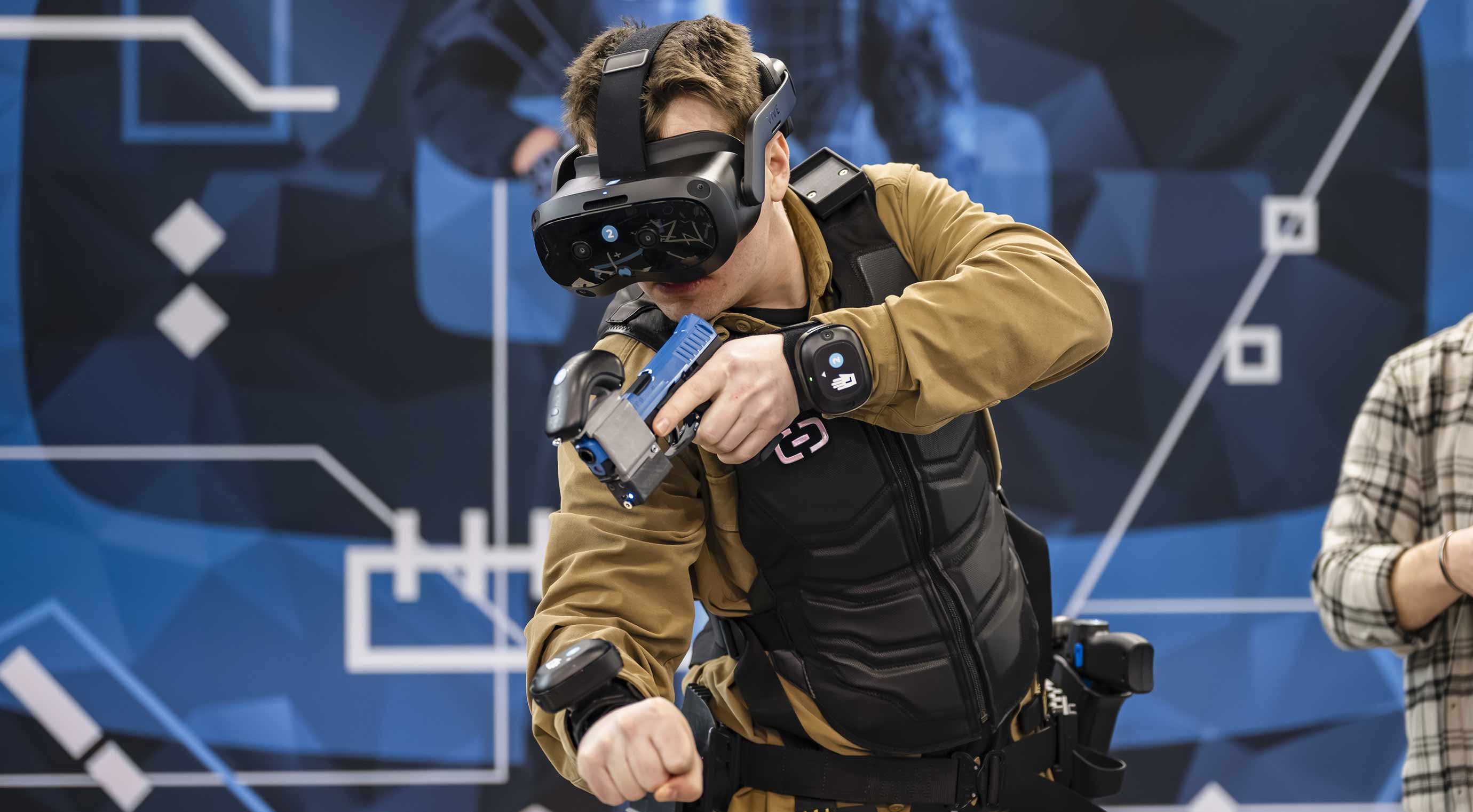 VR-Training auf Messe: Person testet Simulation mit Headset und Trainingswaffe am Stand.